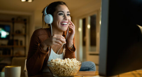 Young woman having fun while eating popcorn and watching movie o