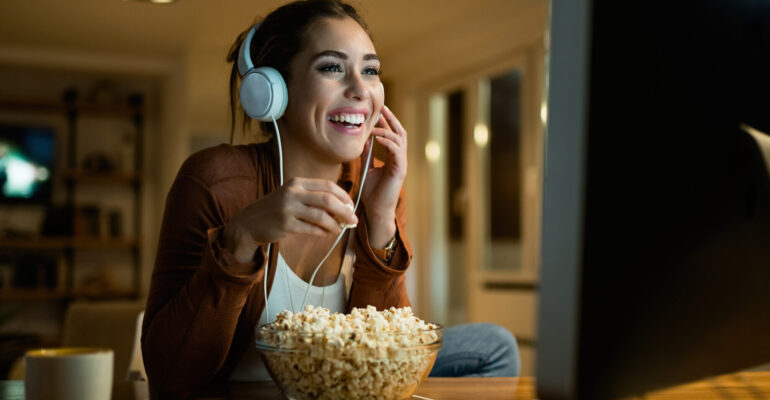 Young woman having fun while eating popcorn and watching movie o