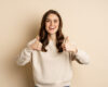 Beautiful young woman, student showing thumbs up in approval, recommending store, standing over beige background