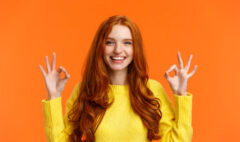 Fashion, shopping, winter holidays concept. Attractive cheerful redhead woman showing okay gestures and smiling, everything alright, approve or like product, recommend online store, orange background