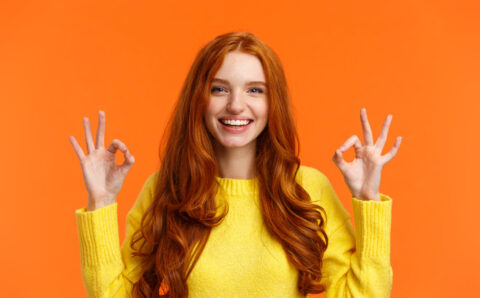 Fashion, shopping, winter holidays concept. Attractive cheerful redhead woman showing okay gestures and smiling, everything alright, approve or like product, recommend online store, orange background