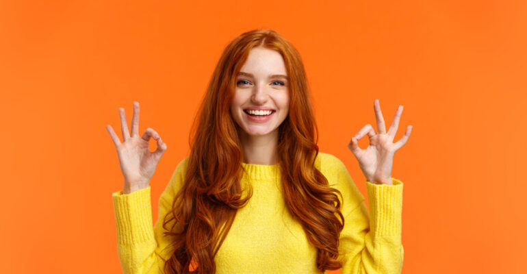 Fashion, shopping, winter holidays concept. Attractive cheerful redhead woman showing okay gestures and smiling, everything alright, approve or like product, recommend online store, orange background