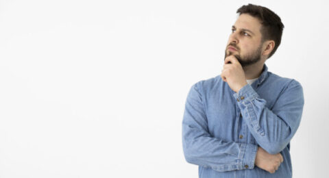 A thoughtful man in a denim shirt looking up, symbolizing curiosity and reflection about learning Brazilian Portuguese.