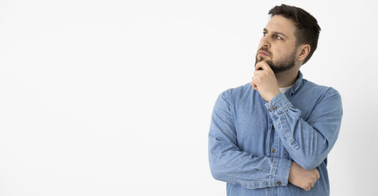 A thoughtful man in a denim shirt looking up, symbolizing curiosity and reflection about learning Brazilian Portuguese.