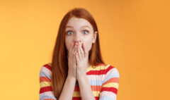 Shocked speechless impressed sensitive redhead european girl reacting stunning rumor gossiping find out secret gasping cover mouth palm stare camera astonished surprised, orange background