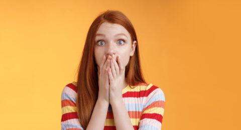 Shocked speechless impressed sensitive redhead european girl reacting stunning rumor gossiping find out secret gasping cover mouth palm stare camera astonished surprised, orange background