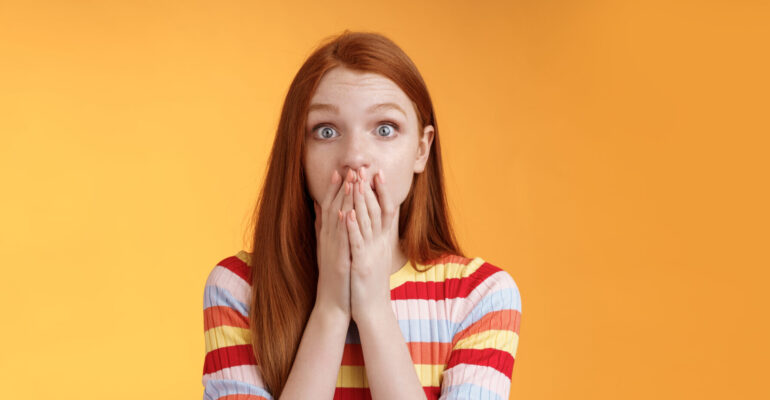 Shocked speechless impressed sensitive redhead european girl reacting stunning rumor gossiping find out secret gasping cover mouth palm stare camera astonished surprised, orange background