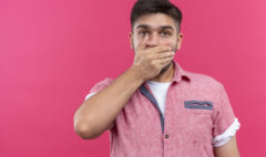 young handsome guy wearing pink polo shirt looking shocked at camera standing over pink background