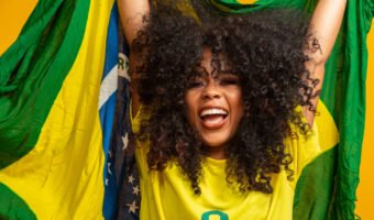 Afro girl cheering for favorite brazilian team, holding national flag in yellow background.