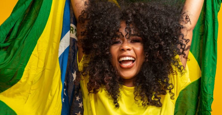 Afro girl cheering for favorite brazilian team, holding national flag in yellow background.